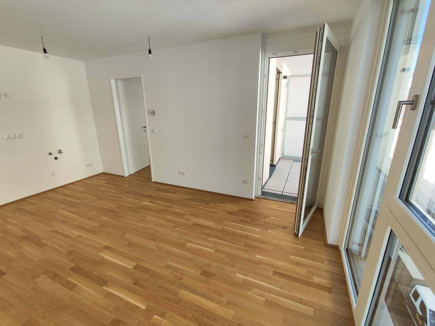 Geräumiges, unmöbliertes Zimmer mit hellem Parkettboden und direktem Zugang zu einem Außenbereich.