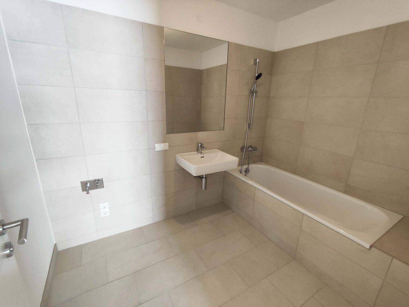 Modernes Badezimmer mit beigefarbenen Fliesen, einer Badewanne und einem wandmontierten Waschbecken.