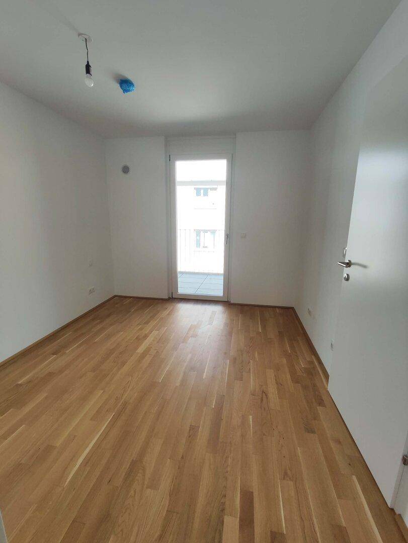 Helles Schlafzimmer mit Parkettboden und Zugang zu einem kleinen Balkon oder einer französischen Brüstung.
