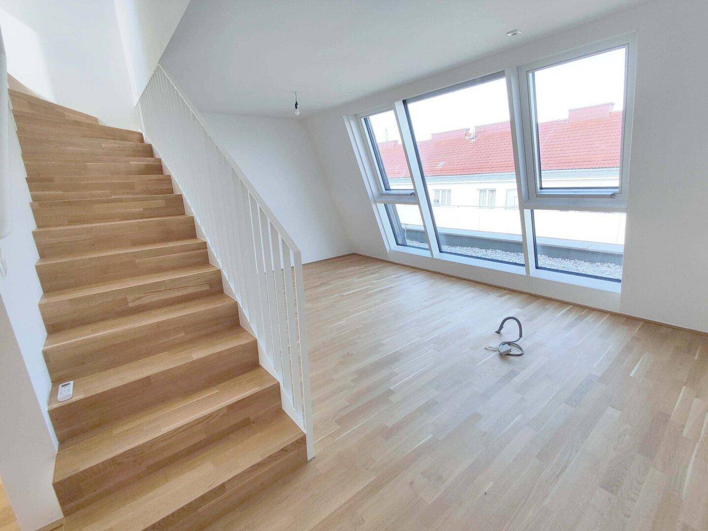 Heller Wohnbereich mit Holzparkettboden, moderner Treppe und großen Dachfenstern.