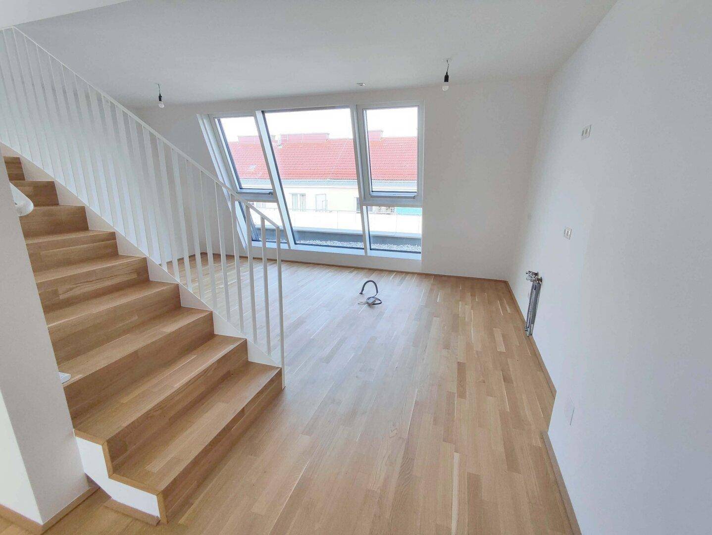 Heller Wohnbereich mit Holzparkettboden, moderner Treppe und großen Dachfenstern.