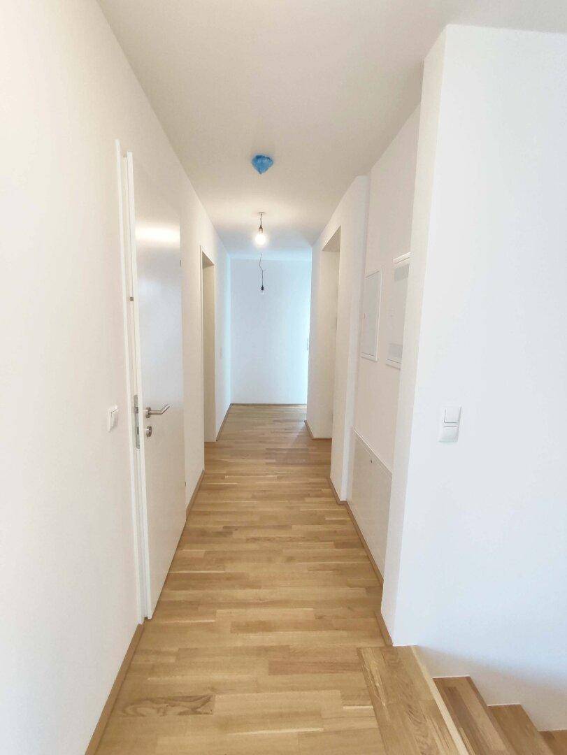 Langer, heller Flur mit Holzparkettboden und weißen Wänden, der zu weiteren Räumen führt.