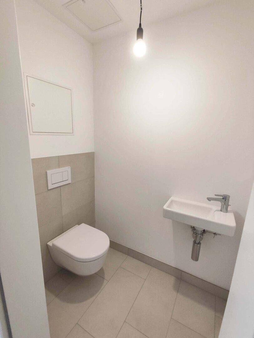 Modernes Gäste-WC mit wandhängendem WC und kleinem Waschbecken, hell gefliest.