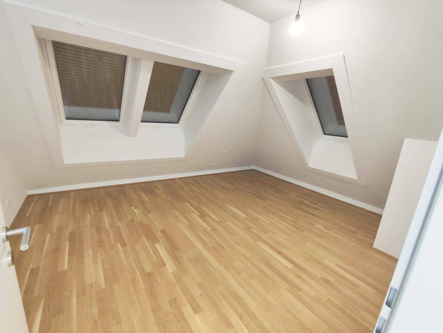 Helles Schlafzimmer mit Holzparkettboden und zwei schrägen Dachfenstern, die viel Licht spenden.