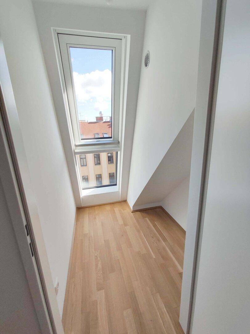 Kleiner, heller Raum mit Holzparkettboden und einem hohen Dachfenster, ideal als Büro.