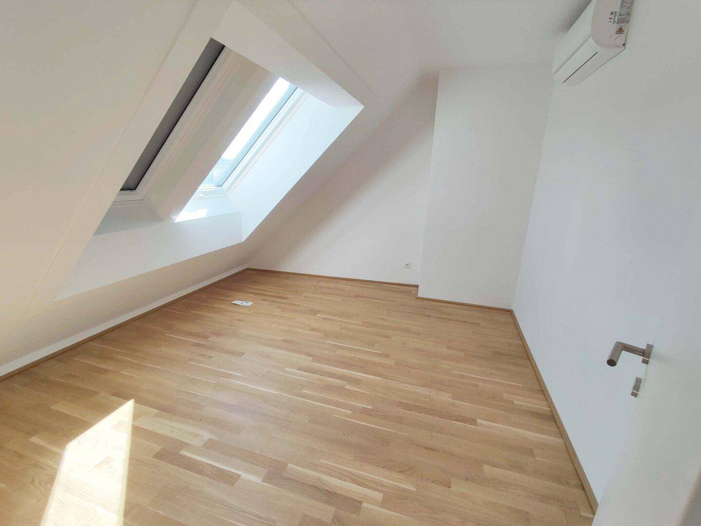 Helles Schlafzimmer mit Holzparkettboden und einem großen Dachfenster, ideal für natürliches Licht.