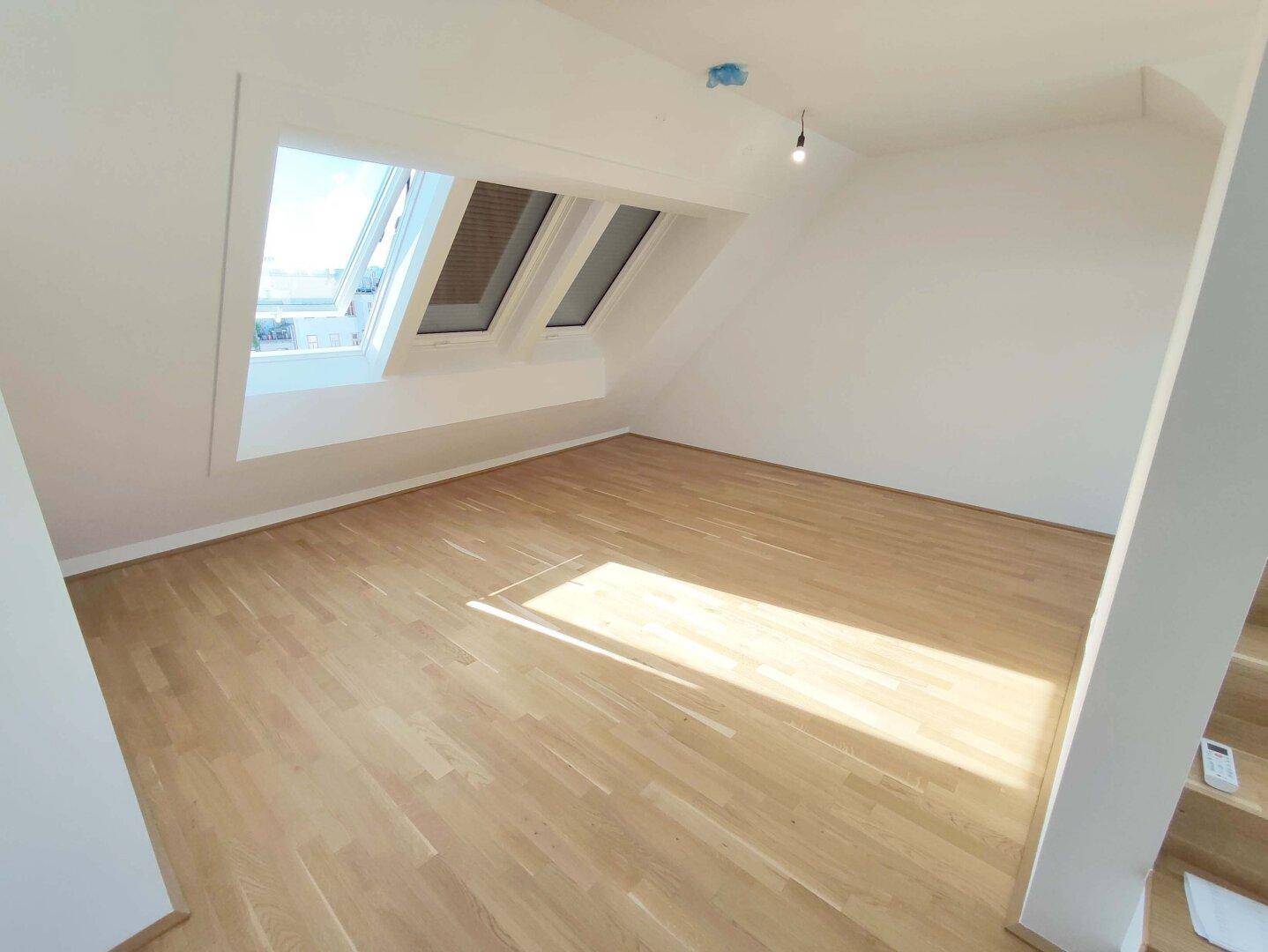 Geräumiges Schlafzimmer mit Holzparkettboden und mehreren Dachfenstern für viel Tageslicht.