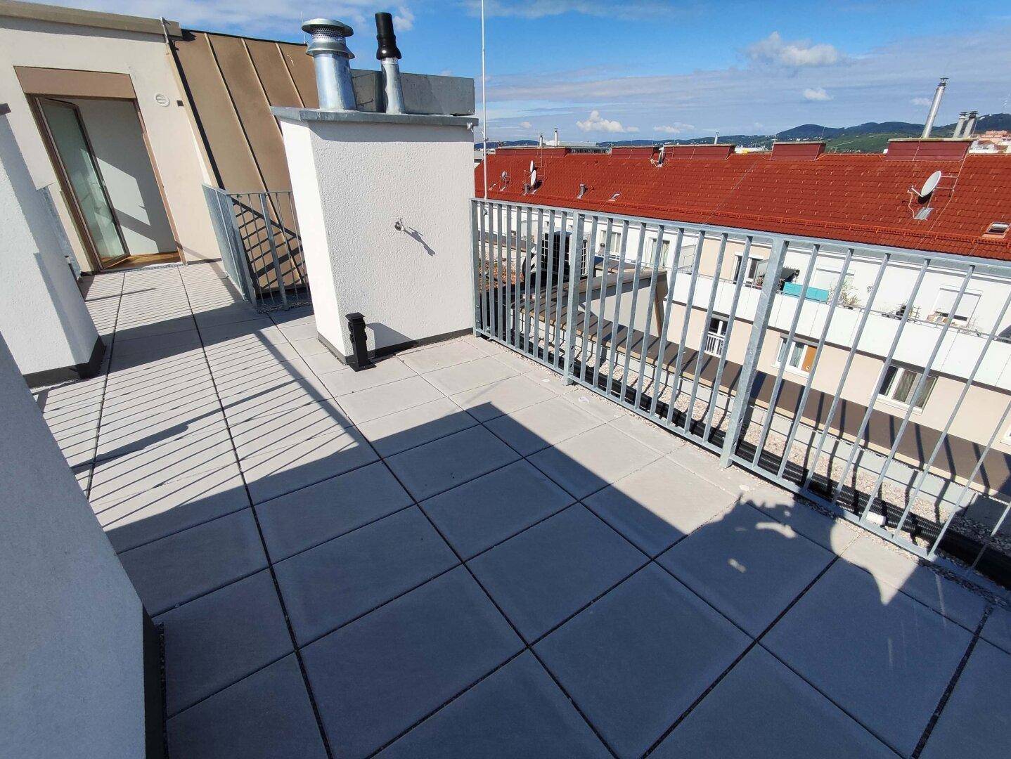 Sonniger Dachterrassenbereich mit Fliesenboden und Blick auf die umliegenden Dächer der Stadt.