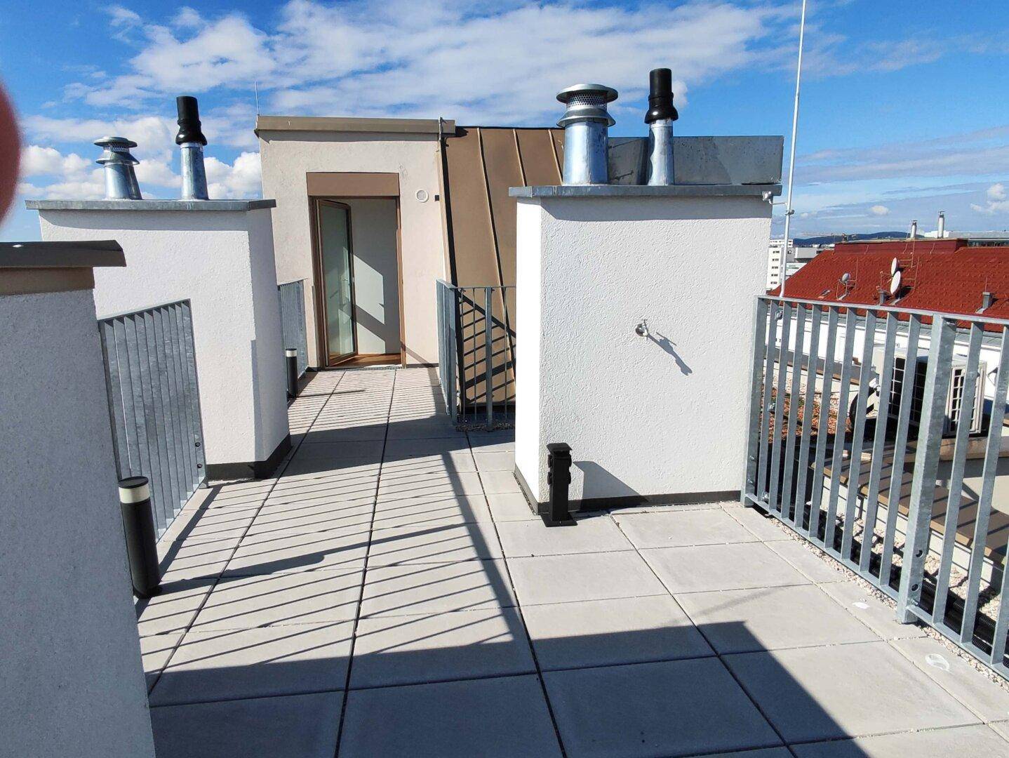 Sonniger Dachterrassenbereich mit Fliesenboden und Blick auf die umliegenden Dächer der Stadt.