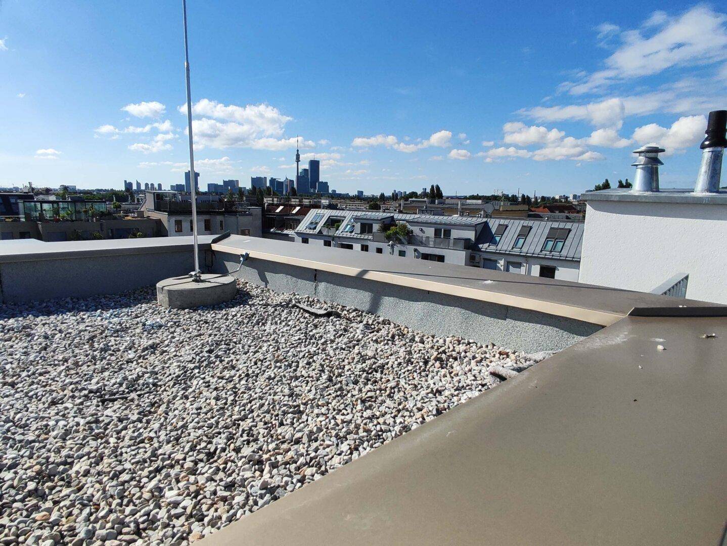 Flachdachbereich mit Kiesbelag und Blick auf die Skyline der Stadt unter blauem Himmel.