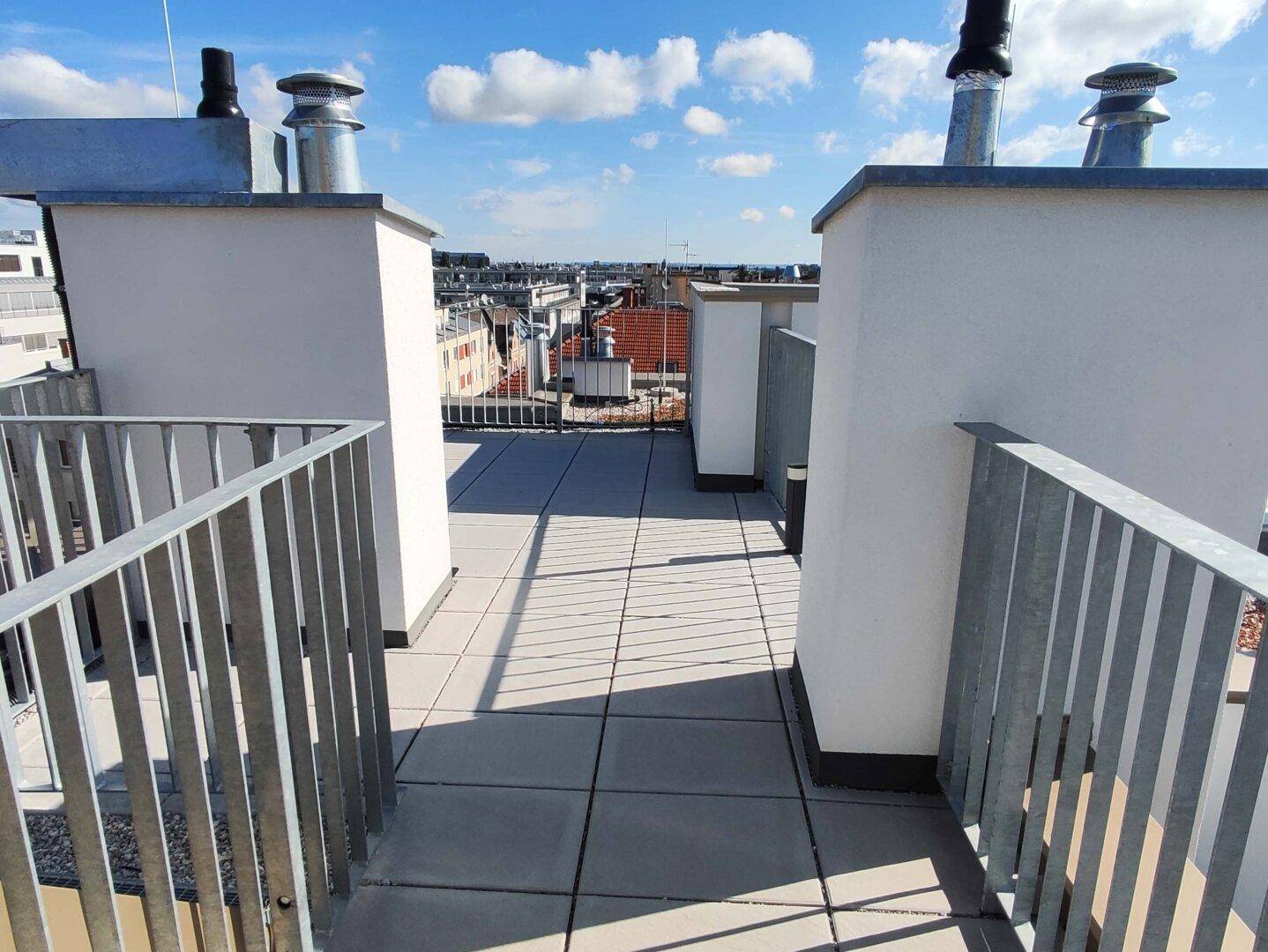 Dachterrasse mit Fliesenboden und Metallgeländer bietet einen weiten Blick über die Stadt.