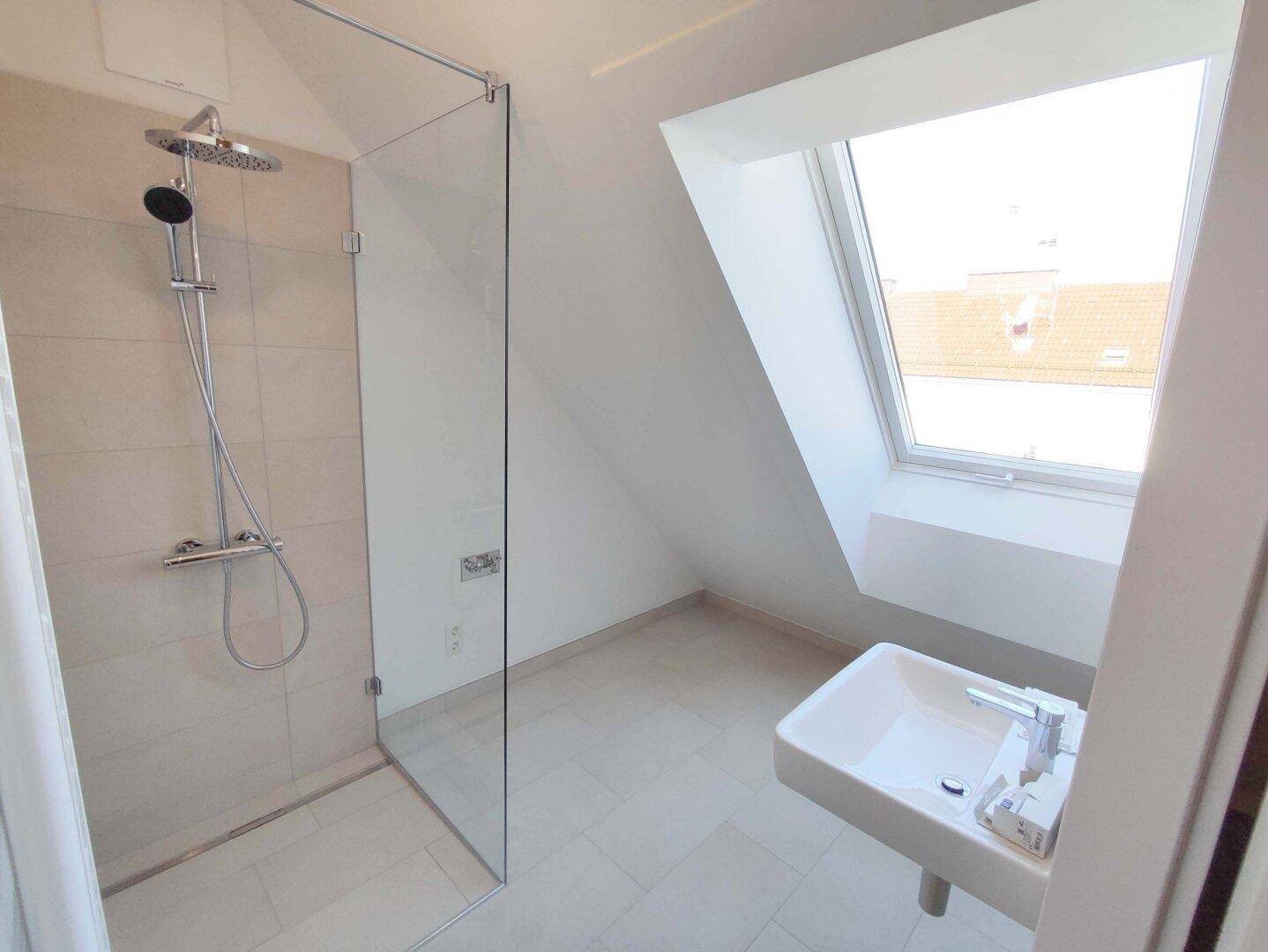 Modernes Badezimmer mit Dusche, Waschbecken und Dachfenster, hell gefliest.