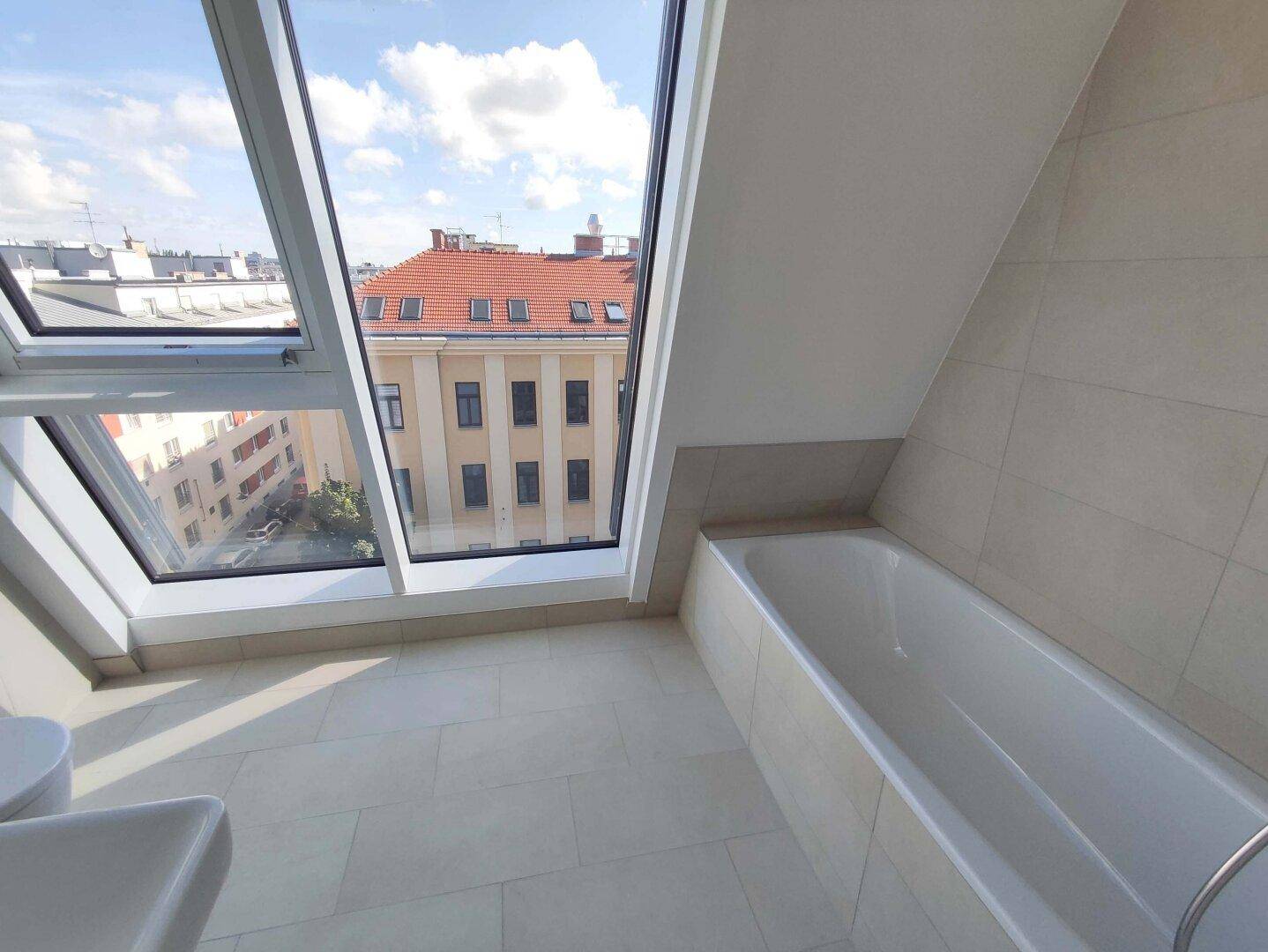 Helles Badezimmer mit Badewanne, Waschbecken und großen Dachfenstern mit Stadtblick.