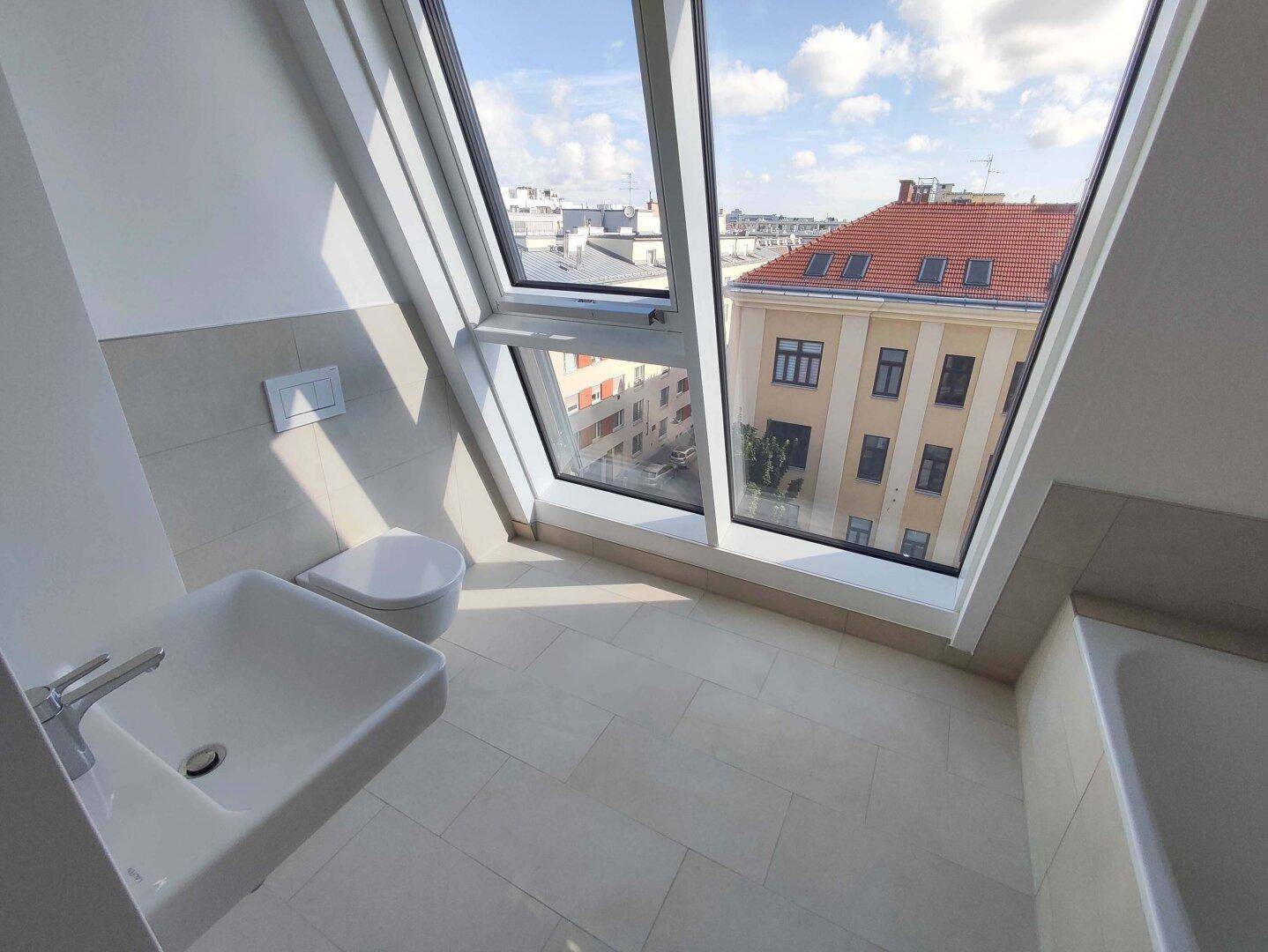 Modernes Badezimmer mit Badewanne, WC und Waschbecken unter großen Dachfenstern mit Stadtblick.
