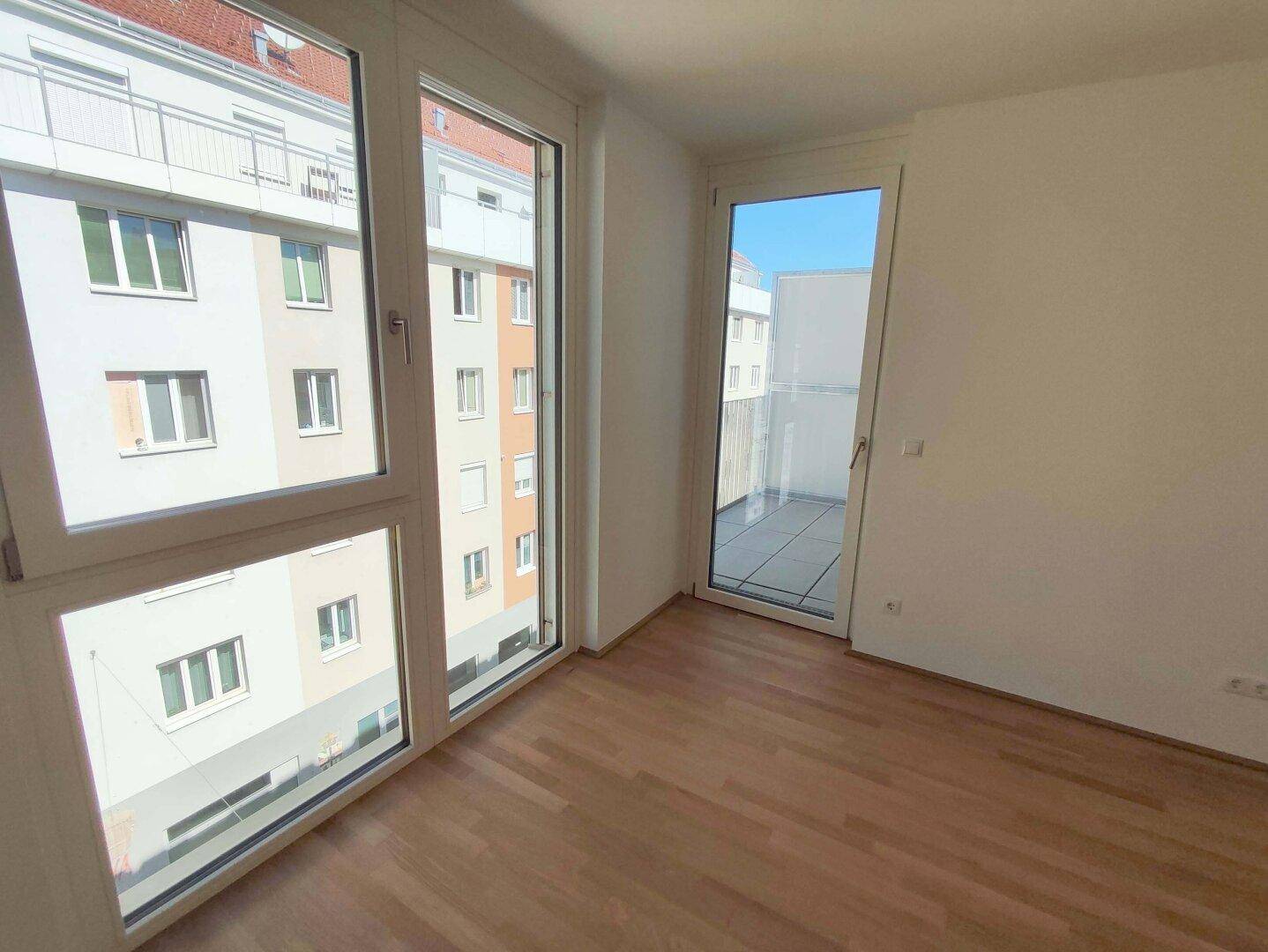 Helles Zimmer mit großen Fenstern, Parkettboden und direktem Zugang zu einem Balkon.