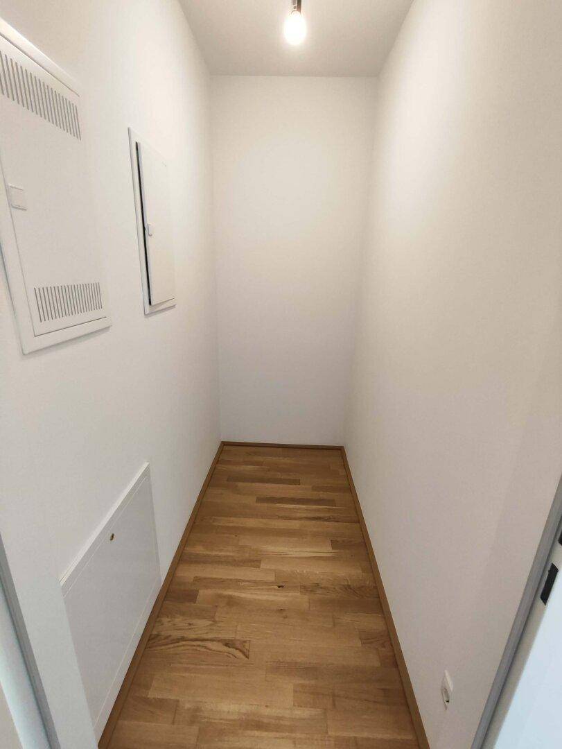 Schmaler Abstellraum mit Parkettboden und weißen Wänden, ideal für Lagerung.