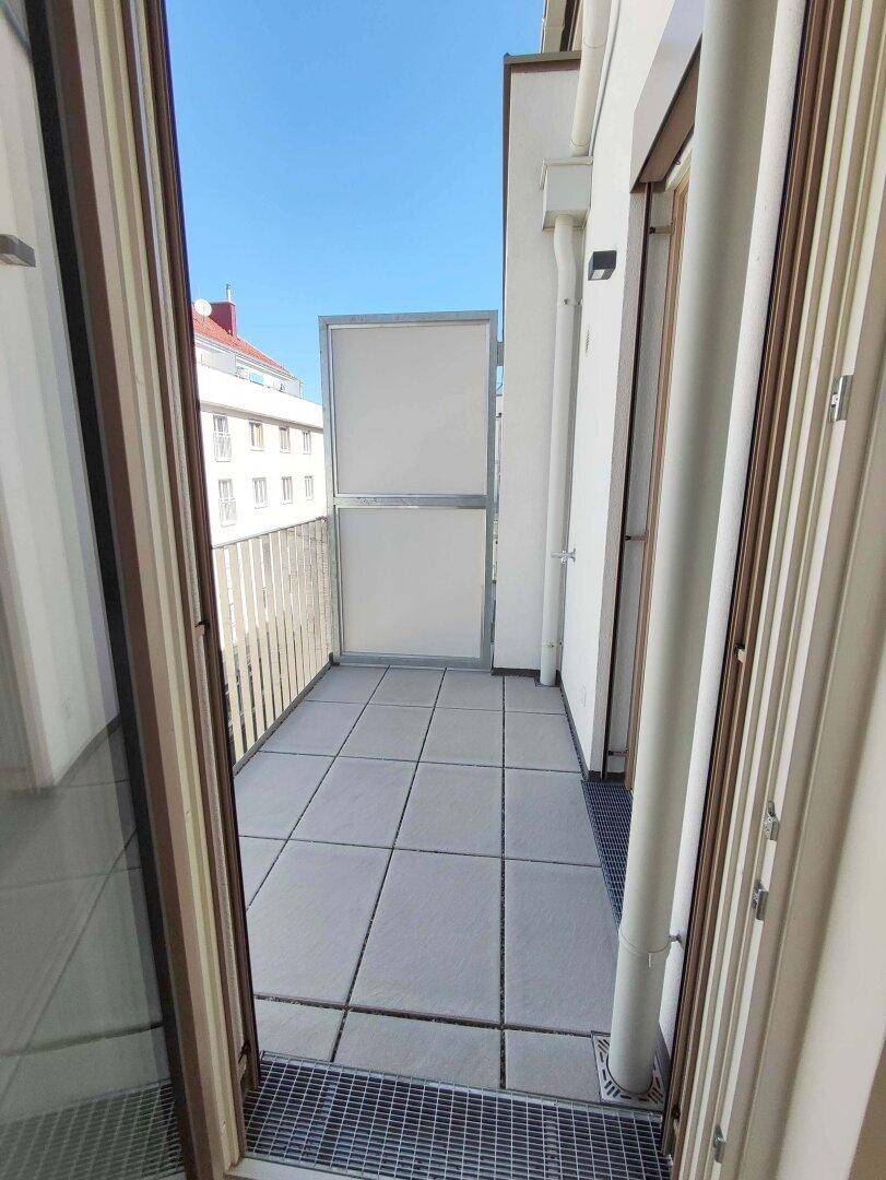 Kleiner, gefliester Balkon mit Metallgeländer und Blick auf umliegende Gebäude.