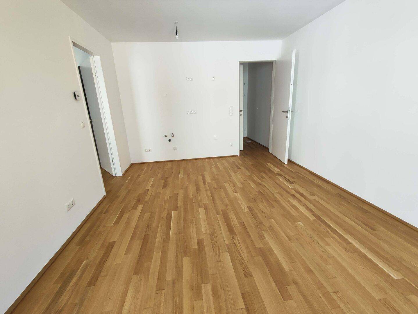 Leerer Küchenbereich mit Anschlüssen für Geräte und hellem Parkettboden.
