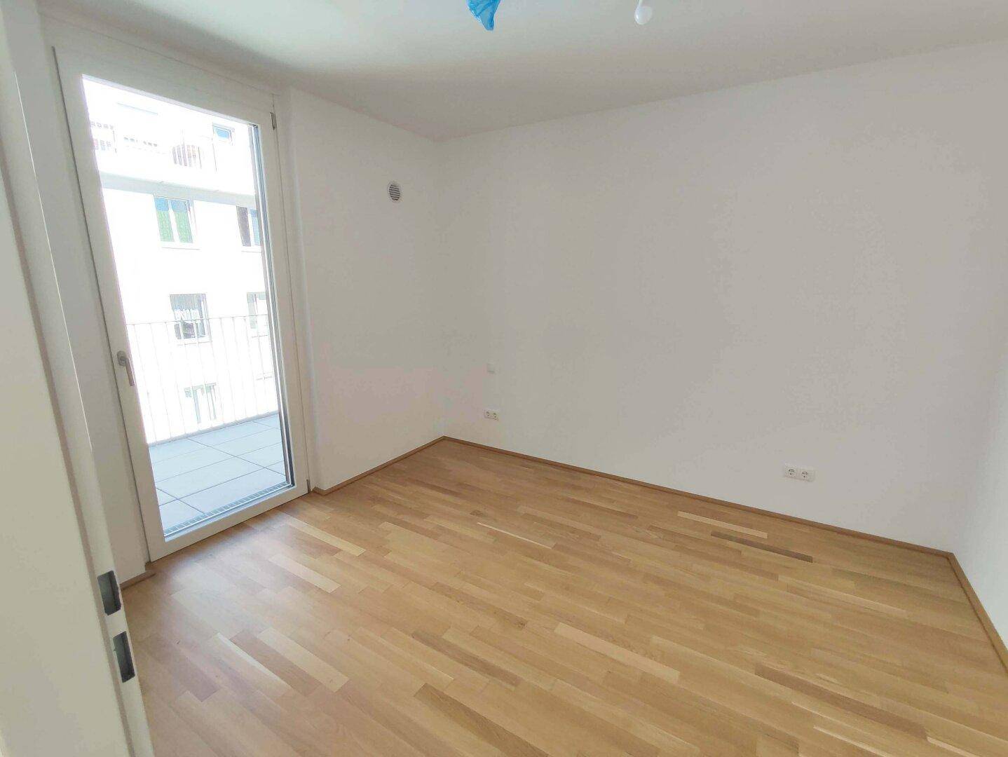 Leeres Zimmer mit Parkettboden und Zugang zu einem Außenbereich, ideal für Schlafzimmer.