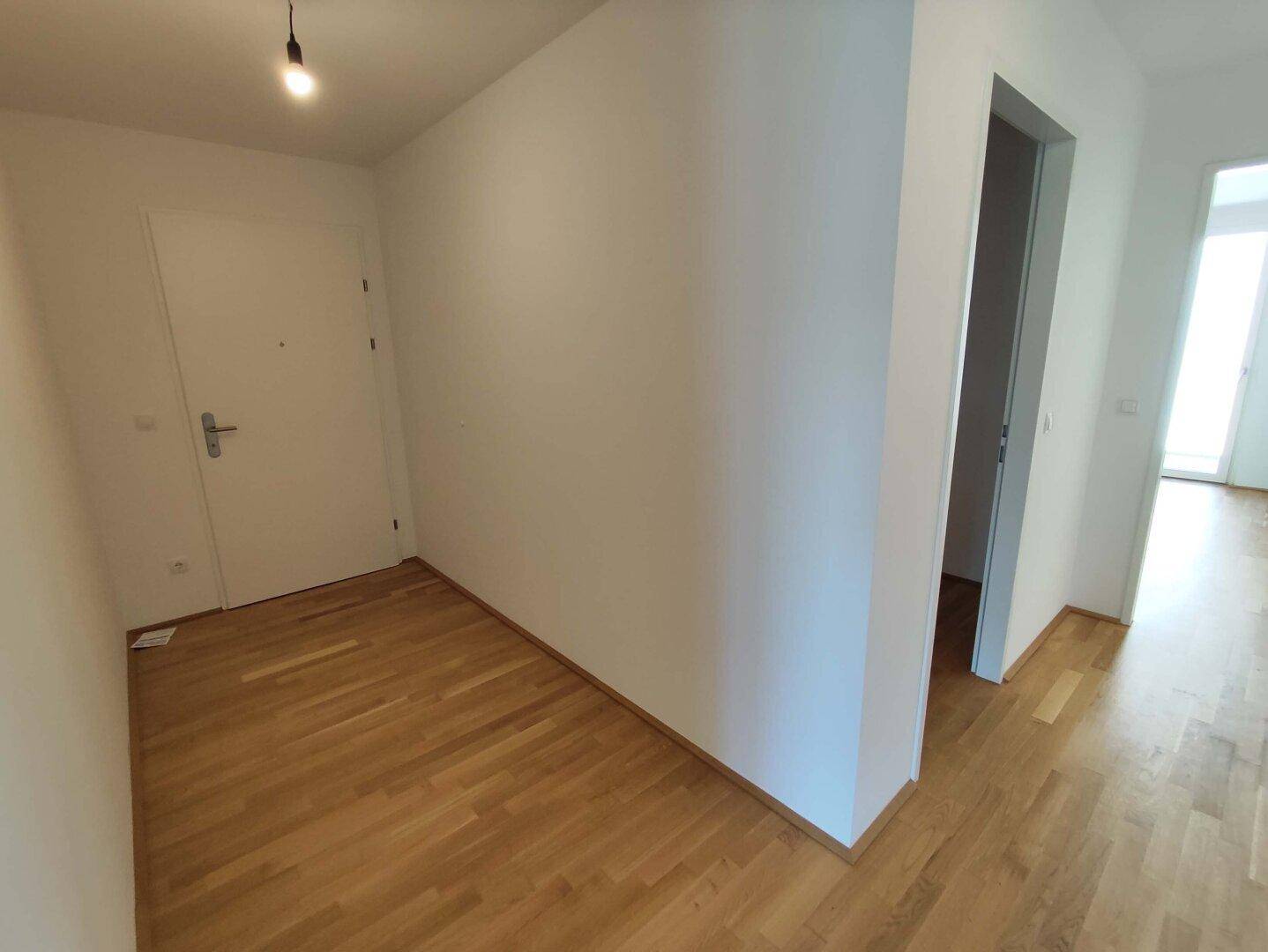 Heller Eingangsbereich mit Parkettboden und weißer Tür, führt zu weiteren Räumen der Wohnung.