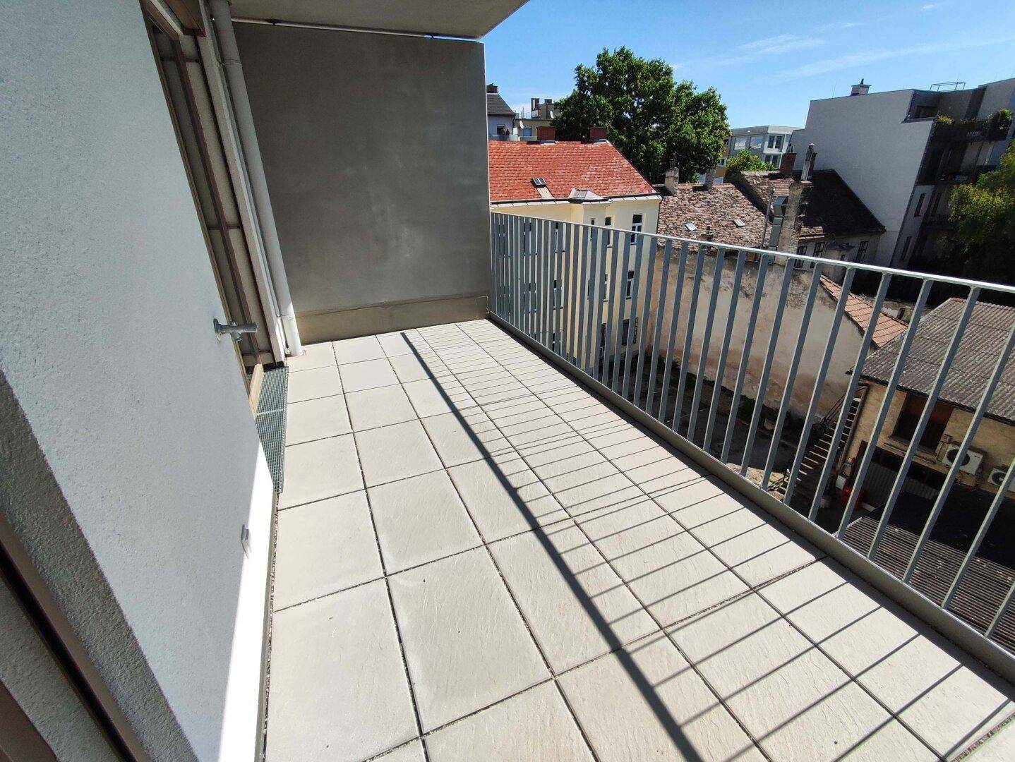 Langer Balkon mit Fliesenboden und Metallgeländer, bietet einen weiten Blick auf die Nachbarschaft.