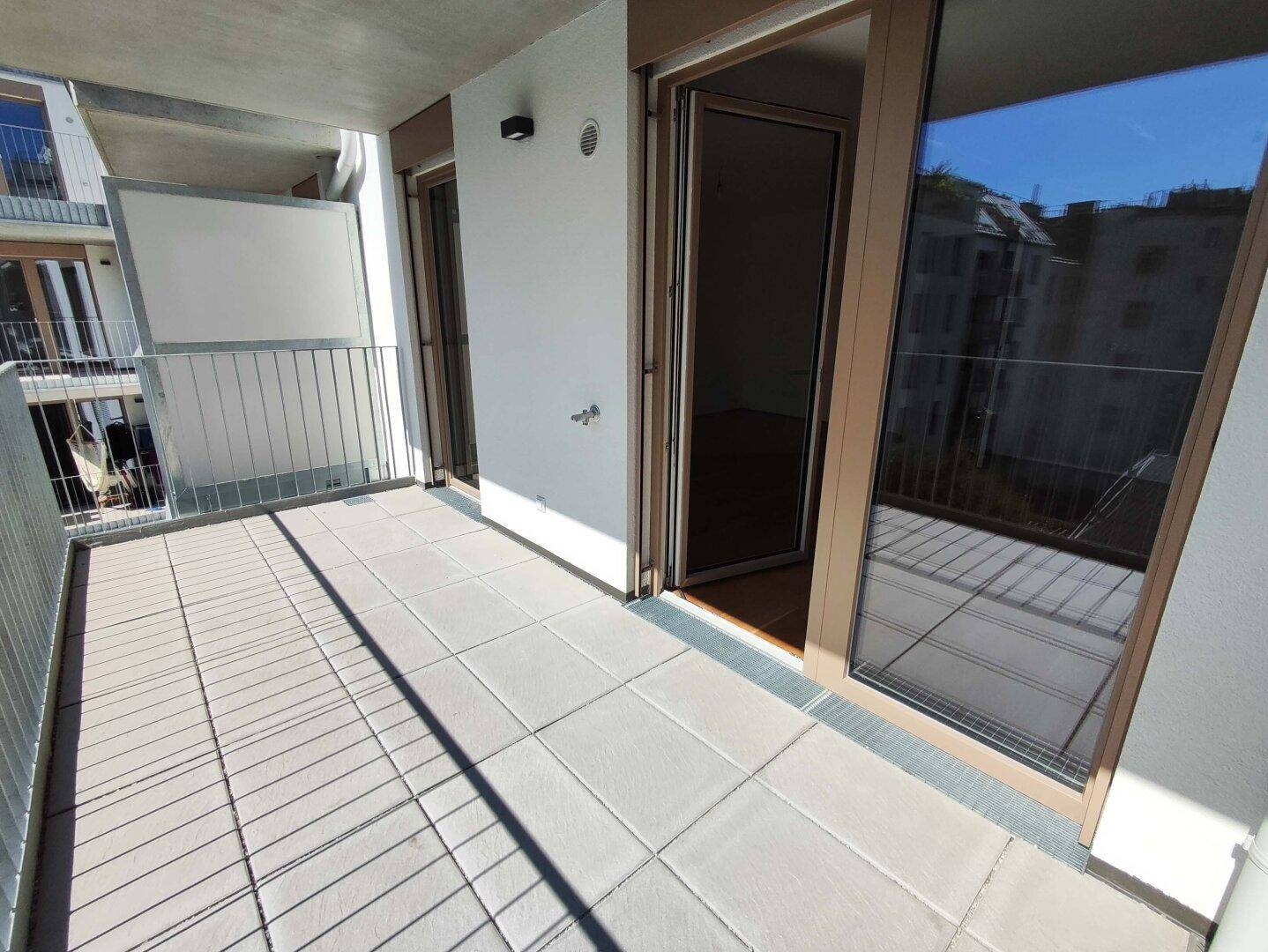 Geräumiger Balkon mit Fliesenboden und Metallgeländer, bietet einen Blick auf die umliegenden Gebäude.