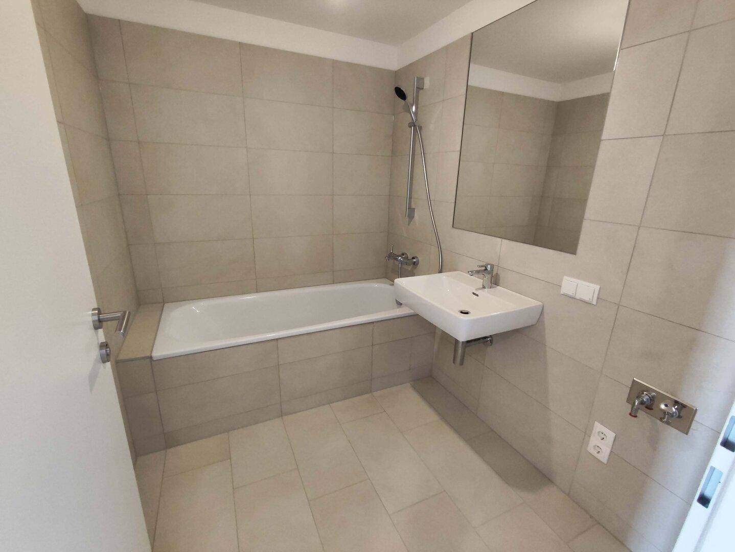 Modernes Badezimmer mit Badewanne, Waschbecken und hellen Fliesen, in neuwertigem Zustand.