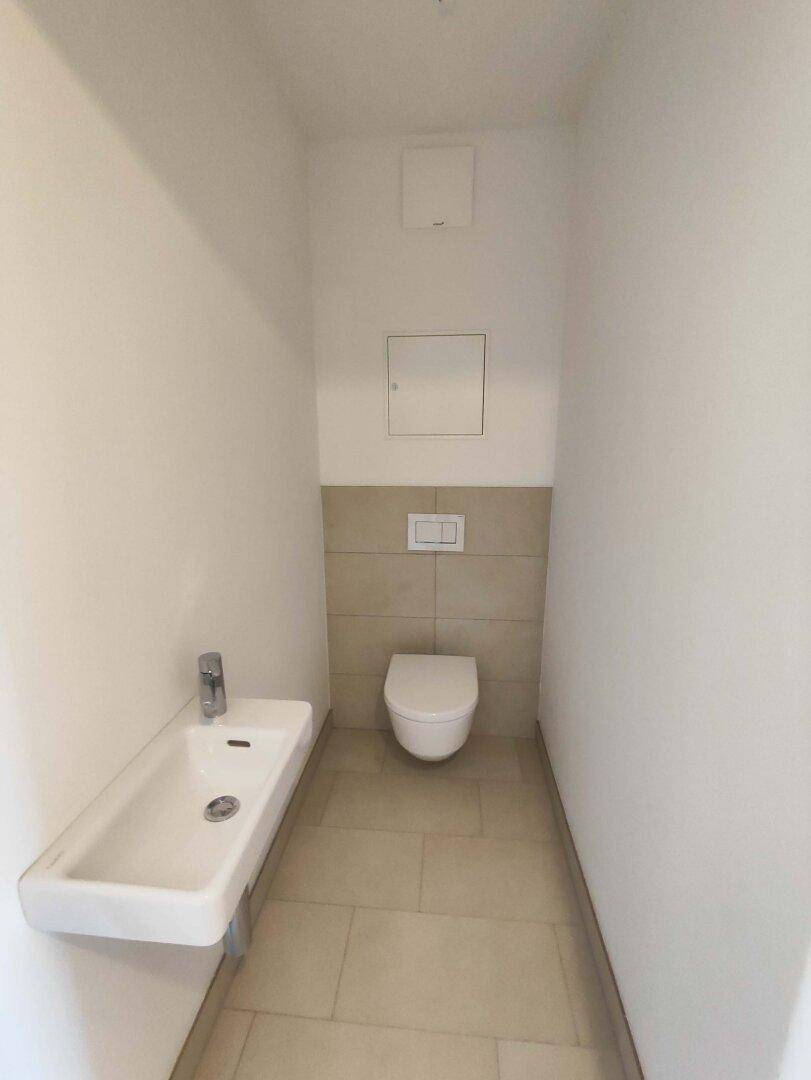 Separates Gäste-WC mit wandhängender Toilette und kleinem Waschbecken, modern gefliest.