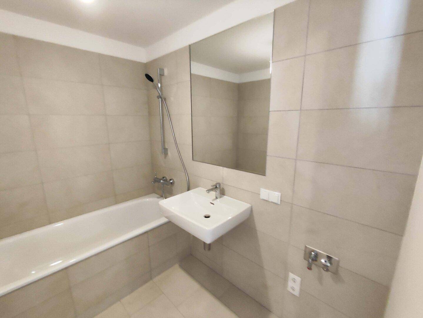 Modernes Badezimmer mit Badewanne, Waschbecken und großem Spiegel, in neuwertigem Zustand.