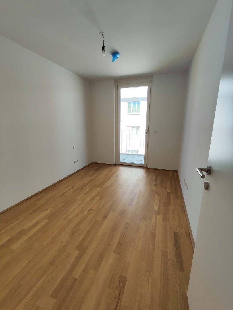 Leeres Schlafzimmer mit Parkettboden und Balkonzugang, ideal für viel Tageslicht und frische Luft.
