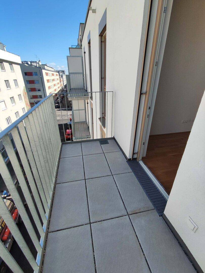 Kleiner Balkon mit Fliesenboden und Blick auf die Stadtstraße und umliegende Gebäude.