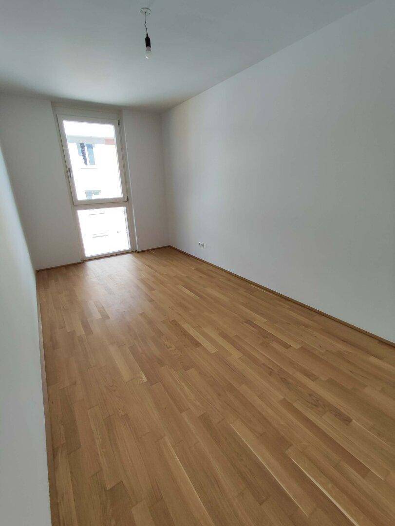 Helles Schlafzimmer mit Parkettboden und einem Fenster, das viel Tageslicht hereinlässt.