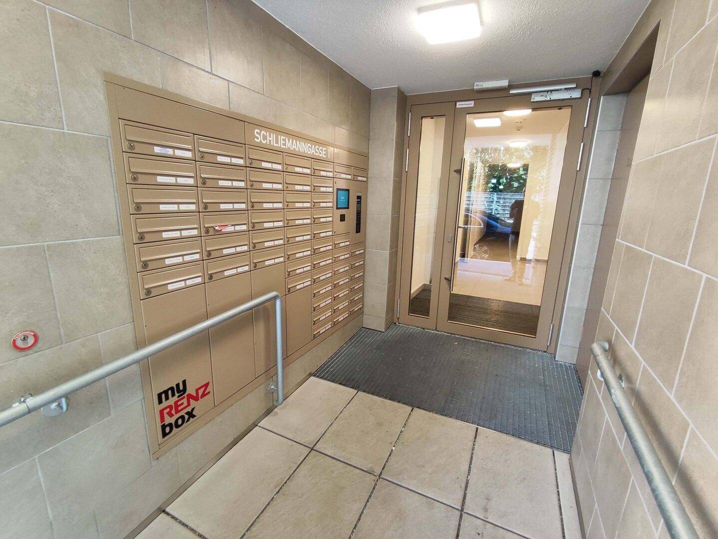 Eingangsbereich mit Briefkastenanlage, Rampe und Glastür zum Gebäude, hell und modern gestaltet.