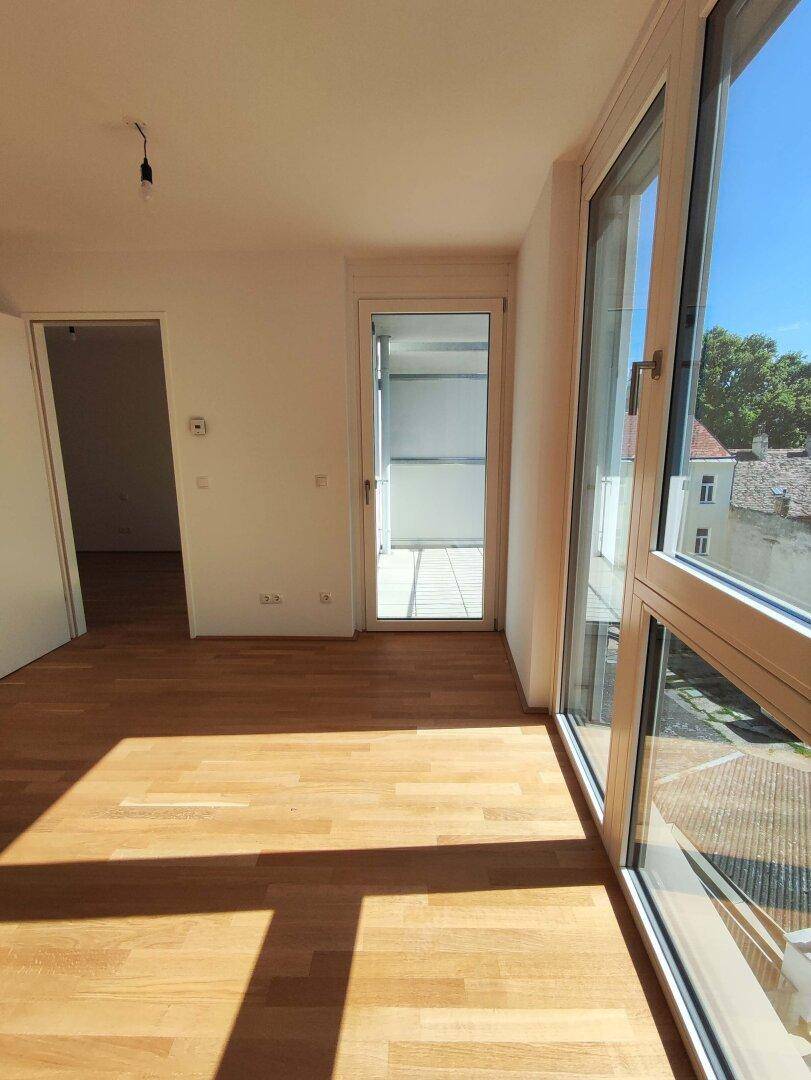 Geräumiger Wohnbereich mit viel Tageslicht durch große Fenster und direktem Zugang zum Balkon.
