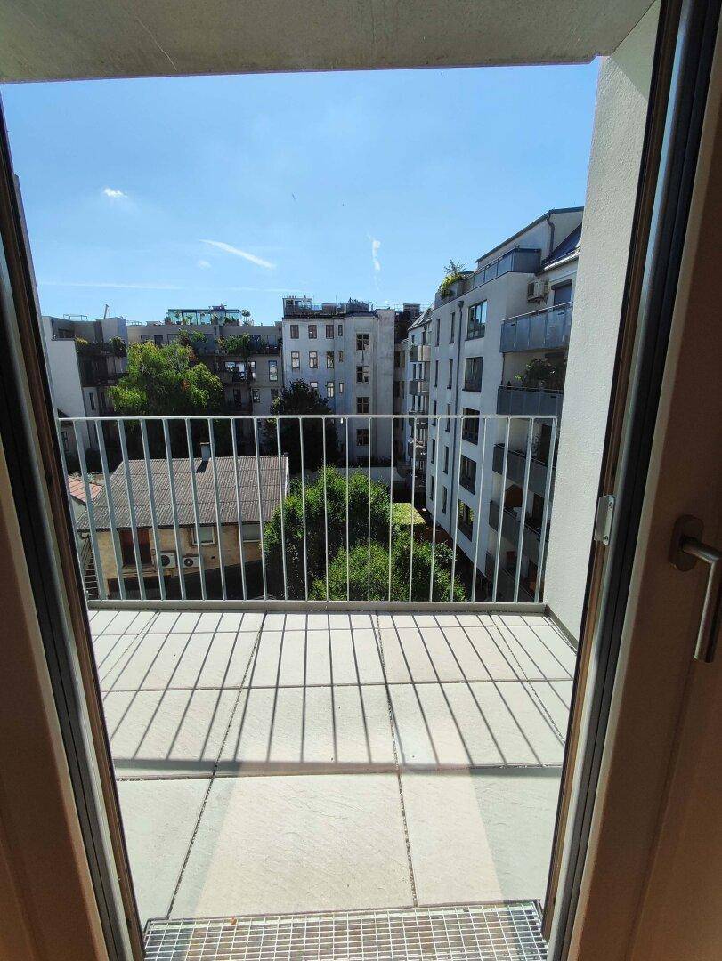 Blick vom Balkon auf die umliegenden Gebäude und grüne Bäume unter strahlend blauem Himmel.