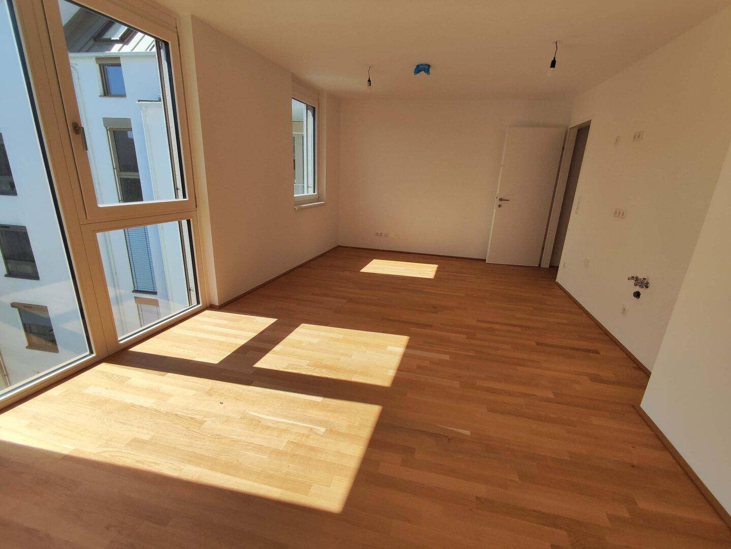 Lichtdurchfluteter Wohnbereich mit hellem Parkettboden und großen Fensterfronten, die viel Tageslicht hereinlassen.