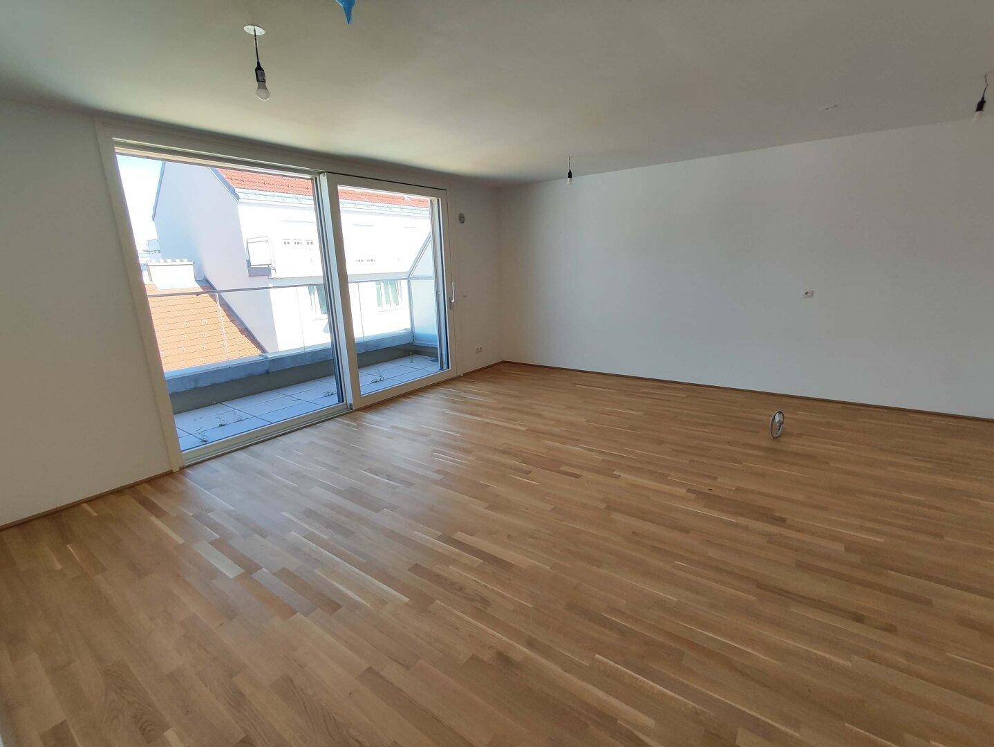 Großer, heller Raum mit Holzboden und breiter Schiebetür, die zu einem Außenbereich führt.
