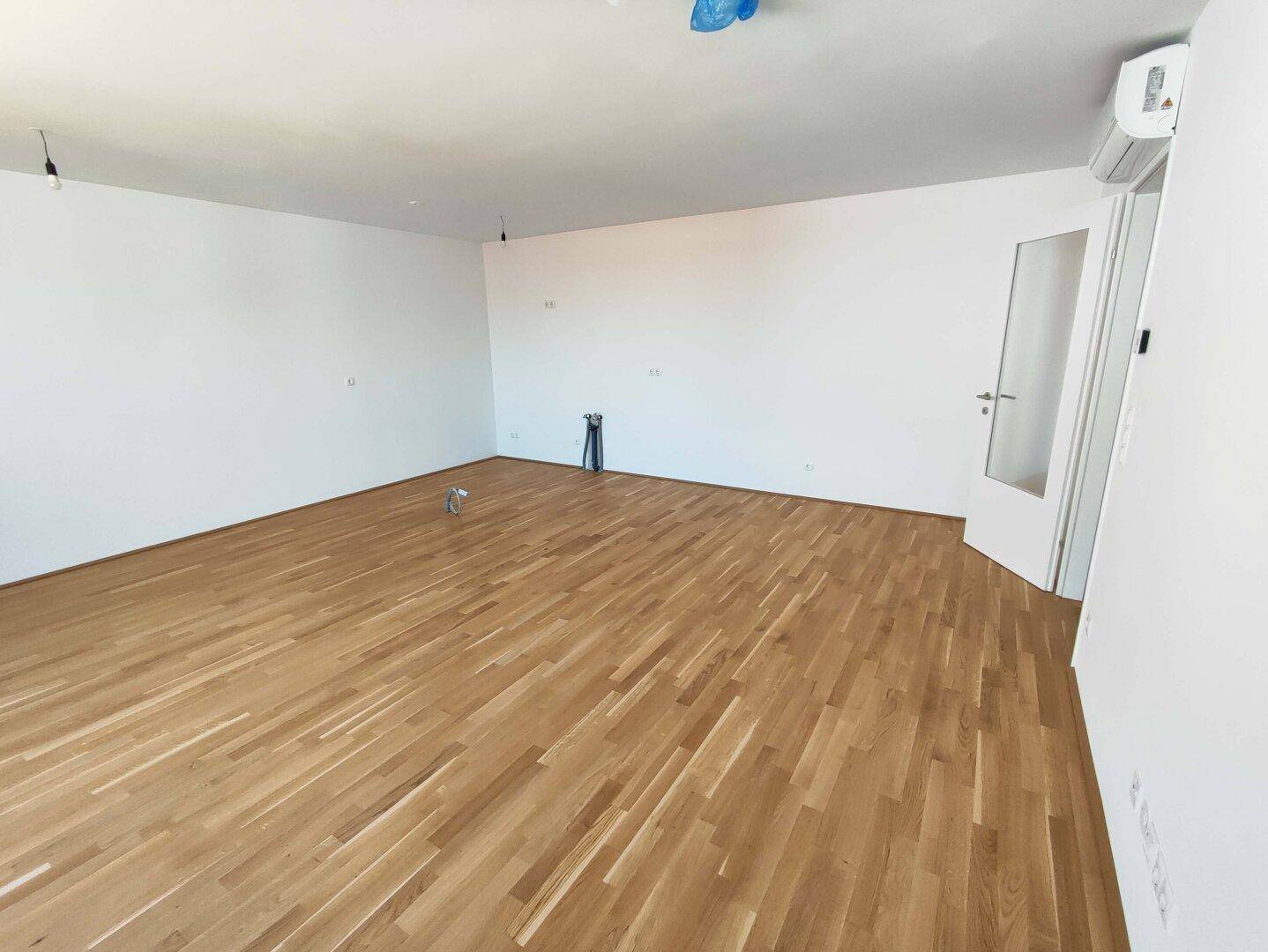 Geräumiger, heller Raum mit Holzboden und Klimaanlage, bereit für die individuelle Gestaltung.