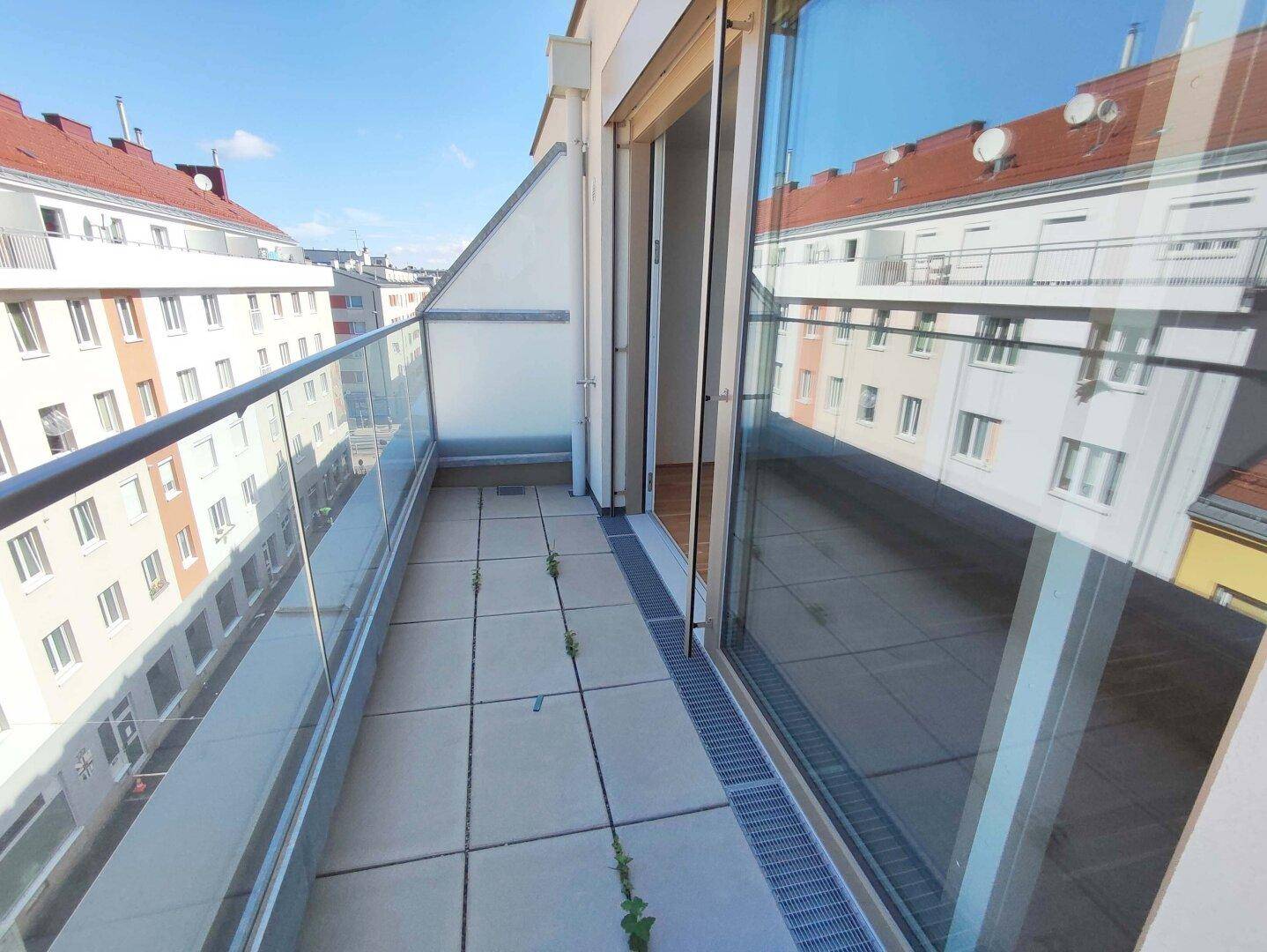 Geräumiger Balkon mit Fliesenboden und Glasgeländer, bietet einen weiten Blick über die Stadt.