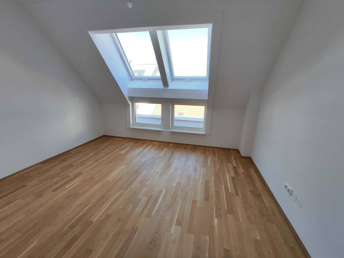 Dachgeschosszimmer mit Holzboden, schrägen Wänden und großen Dachfenstern, die viel Tageslicht hereinlassen.