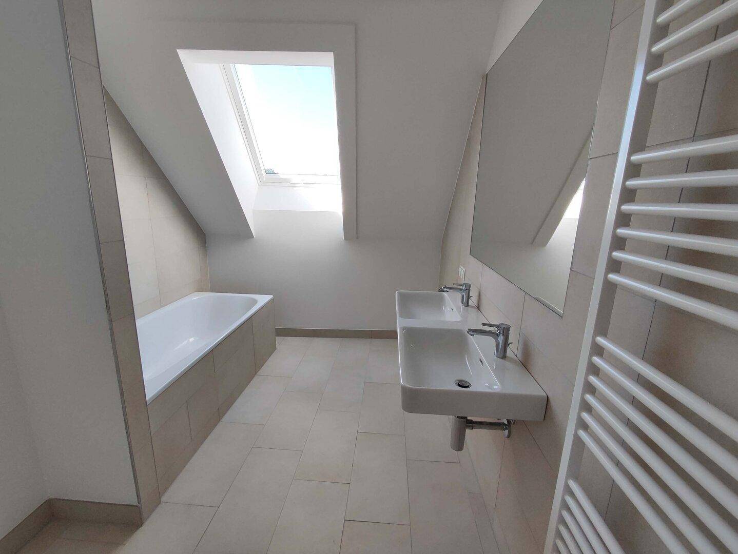 Modernes Badezimmer mit Fliesen, Badewanne, Doppelwaschbecken und Dachfenster unter schräger Decke.