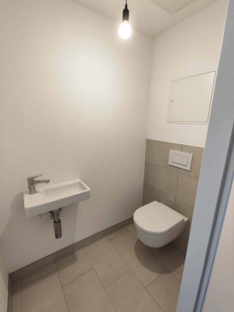 Kleines Gäste-WC mit Fliesenboden, wandhängender Toilette und einem kompakten Waschbecken.