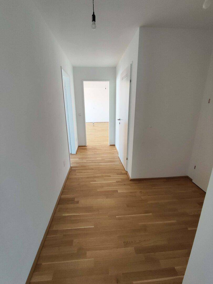 Langer, heller Flur mit Holzboden, der zu den verschiedenen Zimmern der Wohnung führt.