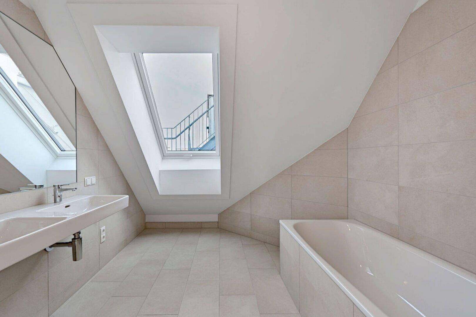 Modernes Badezimmer mit Badewanne, Doppelwaschbecken und Dachfenster unter schräger Decke.