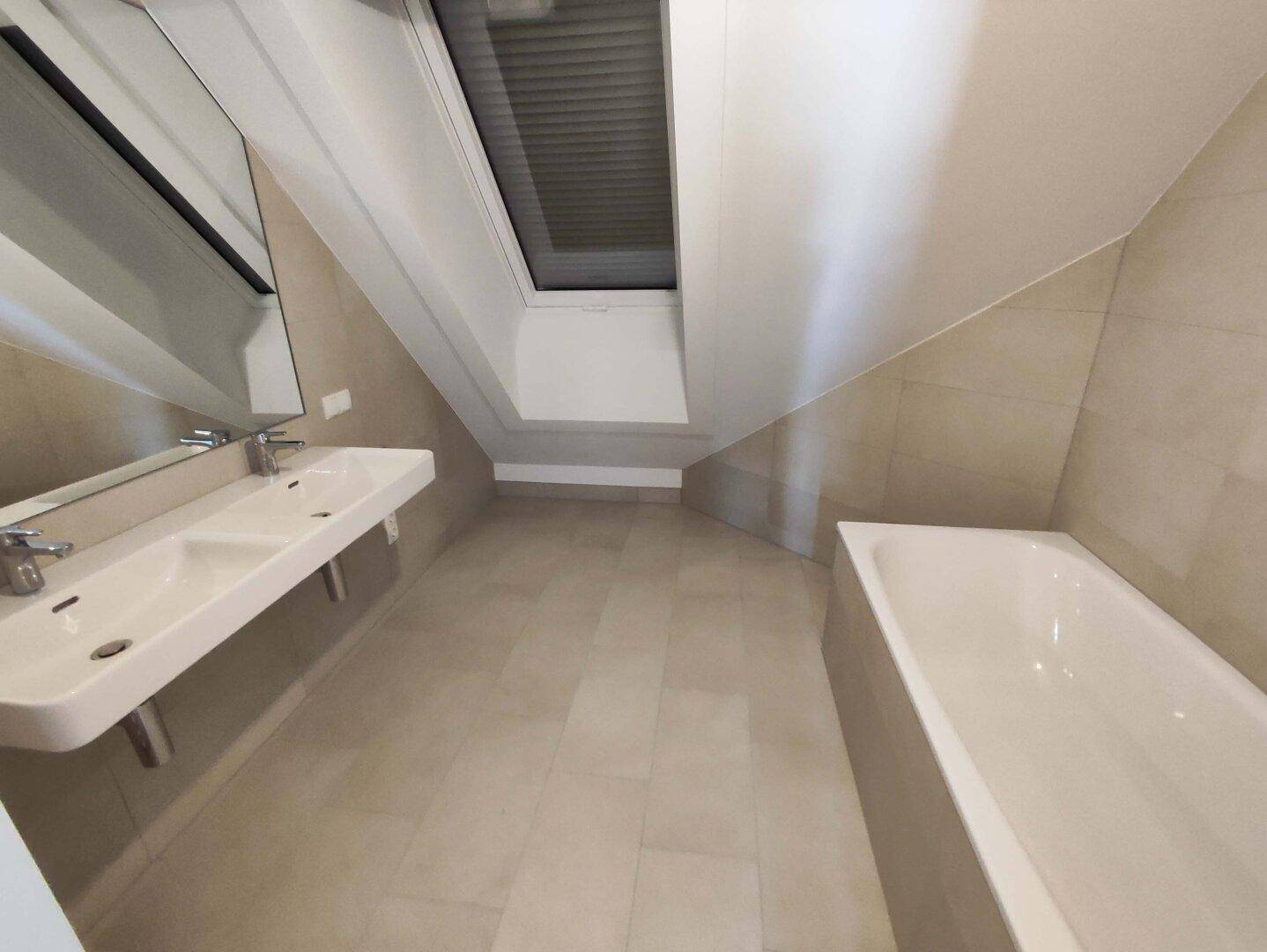 Geräumiges Badezimmer mit Badewanne, Doppelwaschbecken und Dachfenster unter schräger Decke.