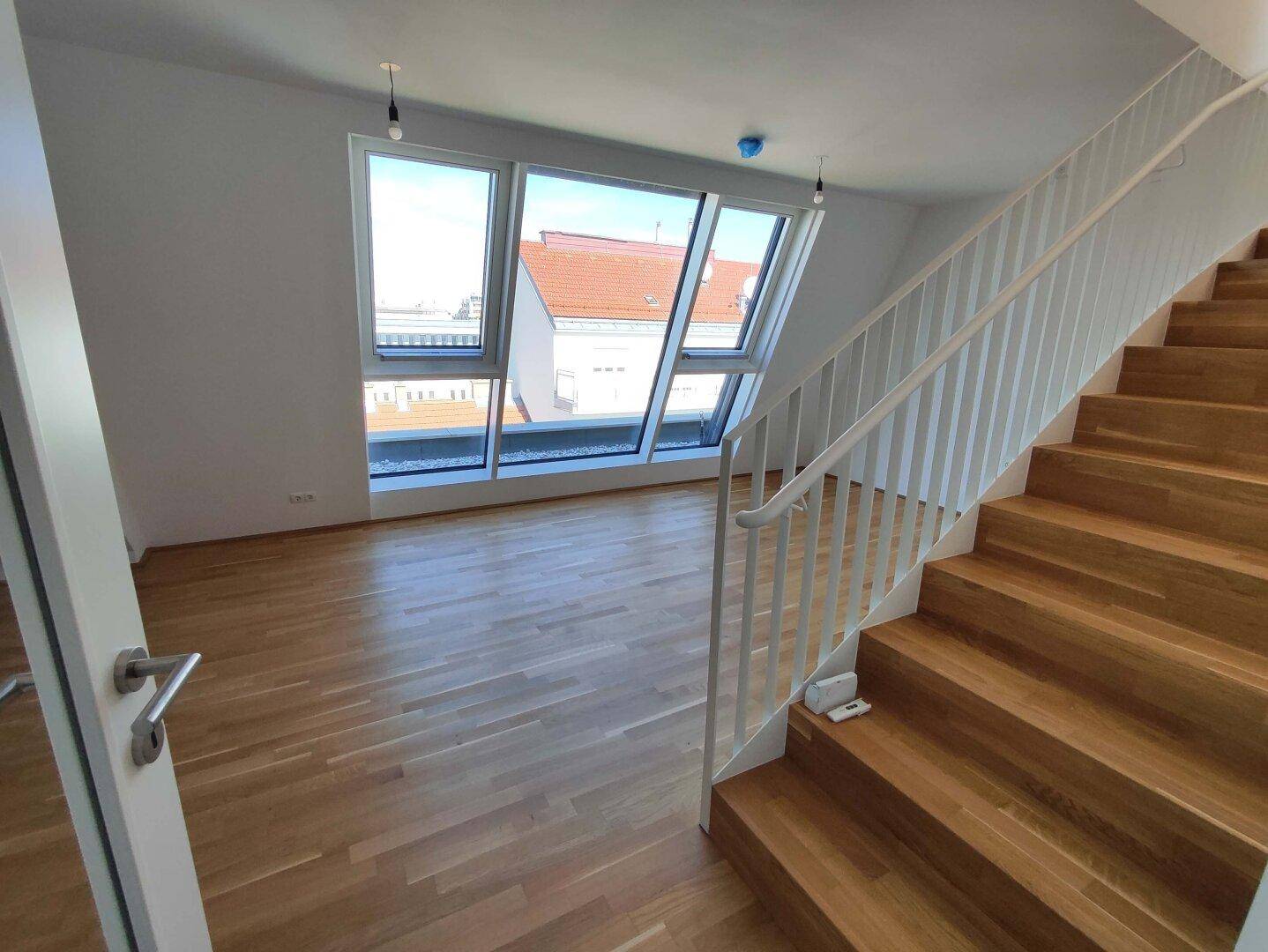 Offener Wohnbereich mit Holztreppe, Parkettboden und großen Fenstern, die eine helle Atmosphäre schaffen.