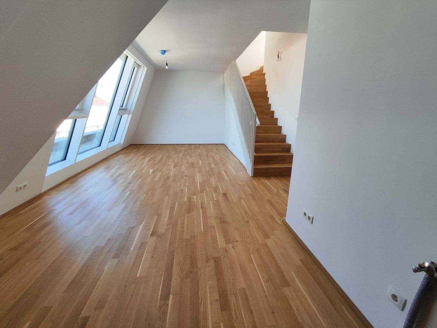 Heller Wohnbereich mit Holztreppe, Parkettboden und großen Fenstern in einem modernen Dachgeschoss.