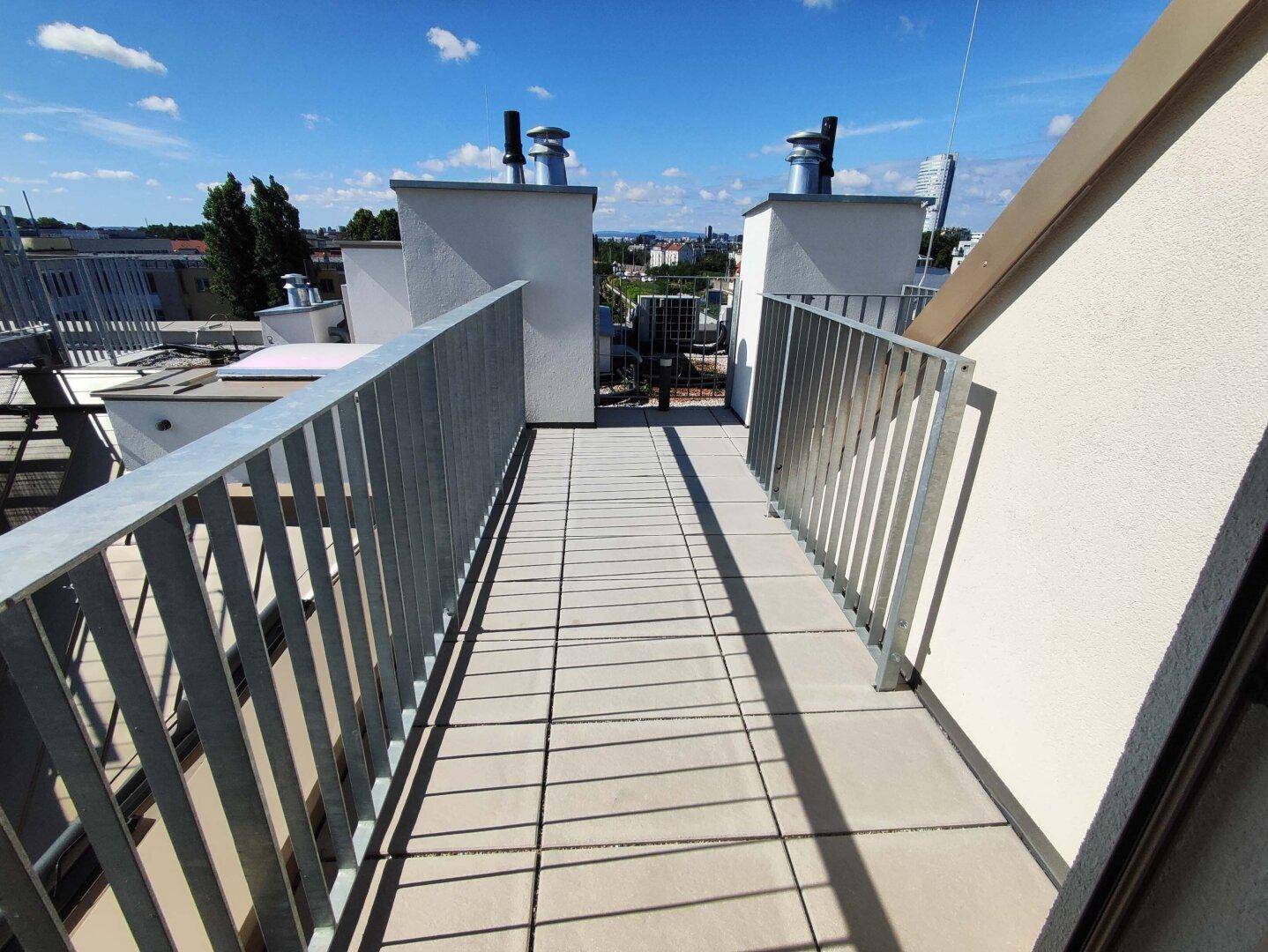 Schmale Dachterrasse mit Fliesenboden und Metallgeländer, bietet eine weite Aussicht über die Stadt.