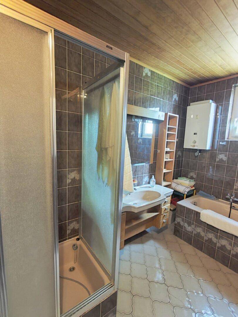 Badezimmer mit braunen Fliesen, Holzdecke, Duschkabine und Badewanne.