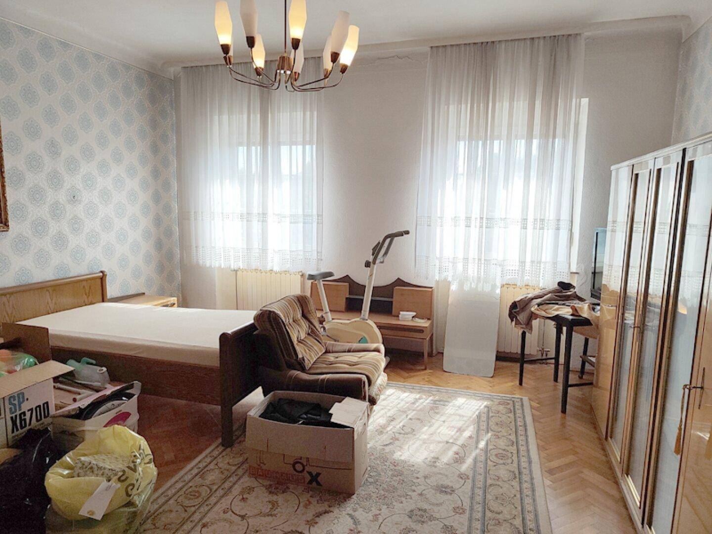 Helles Schlafzimmer mit Parkettboden, zwei Fenstern und einem Bett.